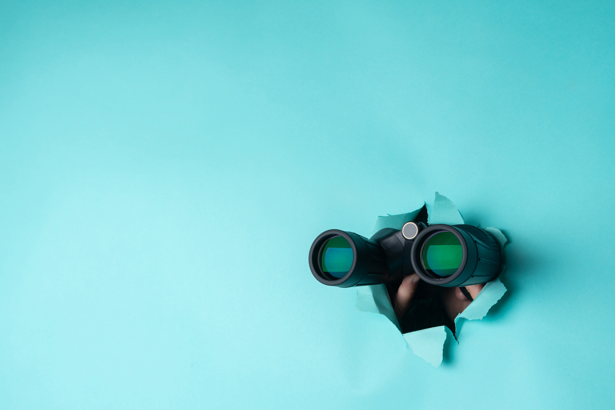 Female hand holds black binoculars on a blue background. Journey, find and search concept. Banner.